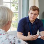 Senior woman talking with male care worker on home visit